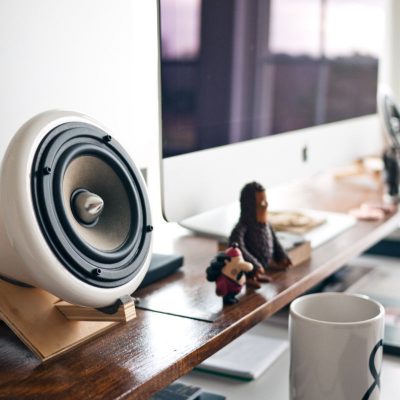 A desk with a monitor, speakers and a cup of coffee.