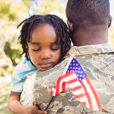 A young boy is hugging his father in a military uniform.