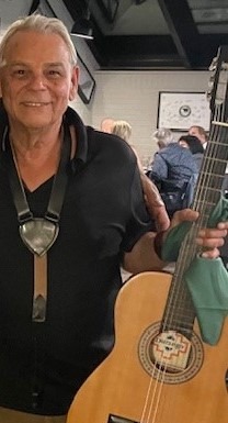 An older man holding a guitar in front of a crowd.