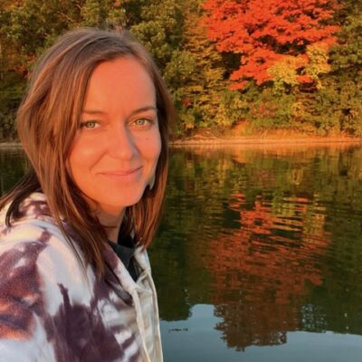 A woman taking a selfie on a boat with trees in the background.