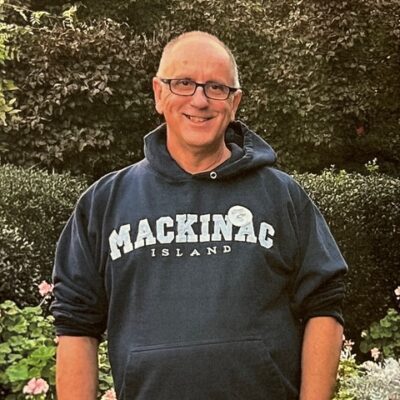 A man in a blue hoodie standing in front of bushes.